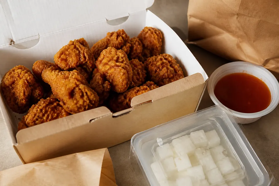Korean fried chicken in an open delivery box with separate sauce and pickled radish containers.